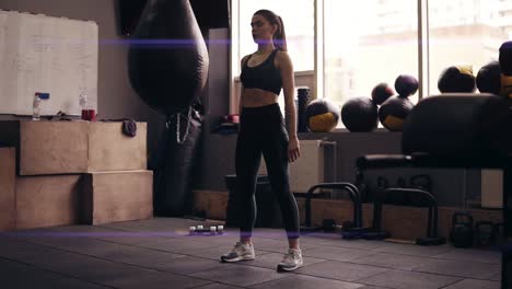 young brunette girl with sportive body wearing black sportswear doing squats at the gym.