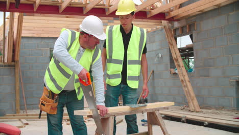 carpintero con aprendiz masculino cortando madera en el sitio de construcción