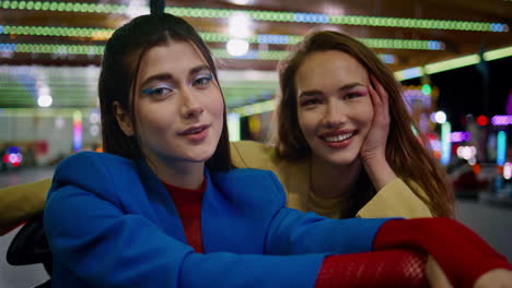 closeup smiling girls posing in amusement park carousel. happy friends sitting