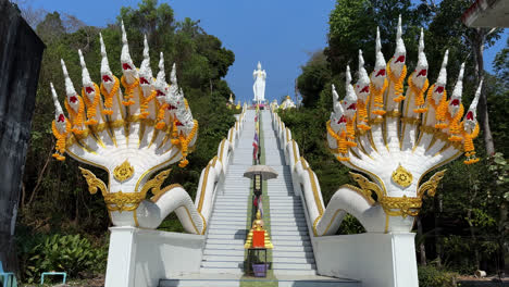 naga staircase with white standing buddha statue on top at wat phlong sawai in rayong, thailand. low angle, static shot