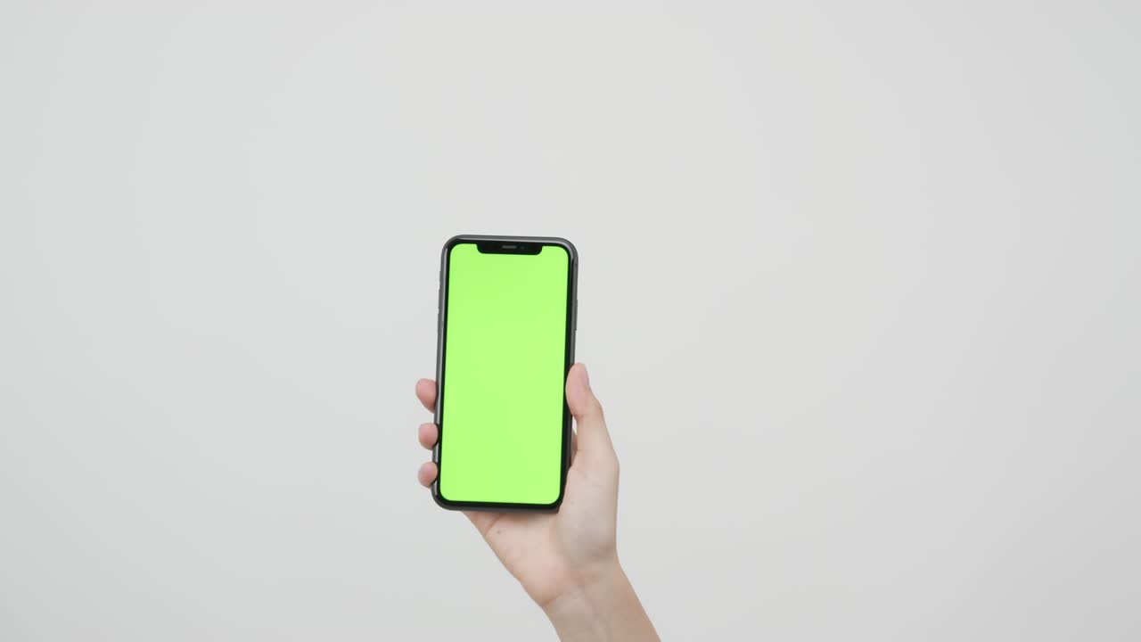Mano che tiene uno smartphone con schermo chroma key e lo mostra su sfondo bianco.