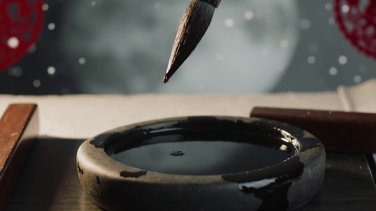 Sænker pensel med bambushåndtag ned i rundt blækhus ved kalligrafibordet og fylder børsterne til skrivning
