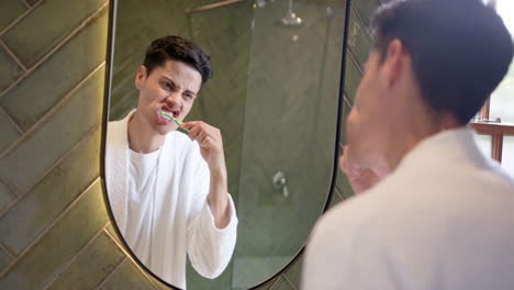 biracial man brushing teeth in morning, looking in bathroom mirror, slow motion