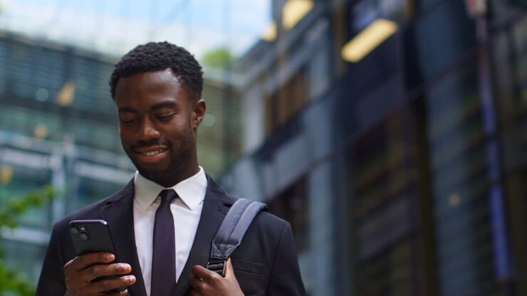 Giovane uomo d'affari in giacca e cravatta che usa lo smartphone fuori dagli uffici nel quartiere finanziario della City di Londra, Regno Unito.
