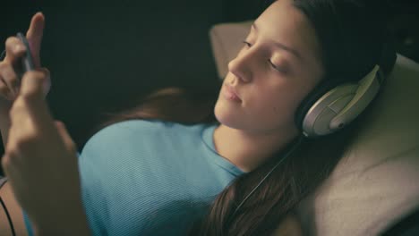 teen girl relaxing at home, listening to music with headphones and using her smartphone. a calm, intimate moment of digital leisure in a cozy setting.