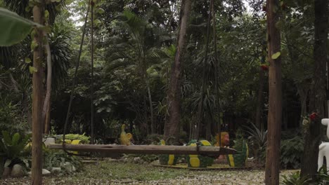 An-empty-swaying-swing-in-the-middle-of-a-tropical-garden,-the-forest-area-surrounded-by-trees-and-fresh-green-foliage-in-Kanchanaburi,-Thailand