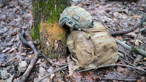 a foreign volunteer soldier's helmet and backpack rest against a tree during a combat training exercise in ukraine. the unit is preparing for frontline deployment against russia