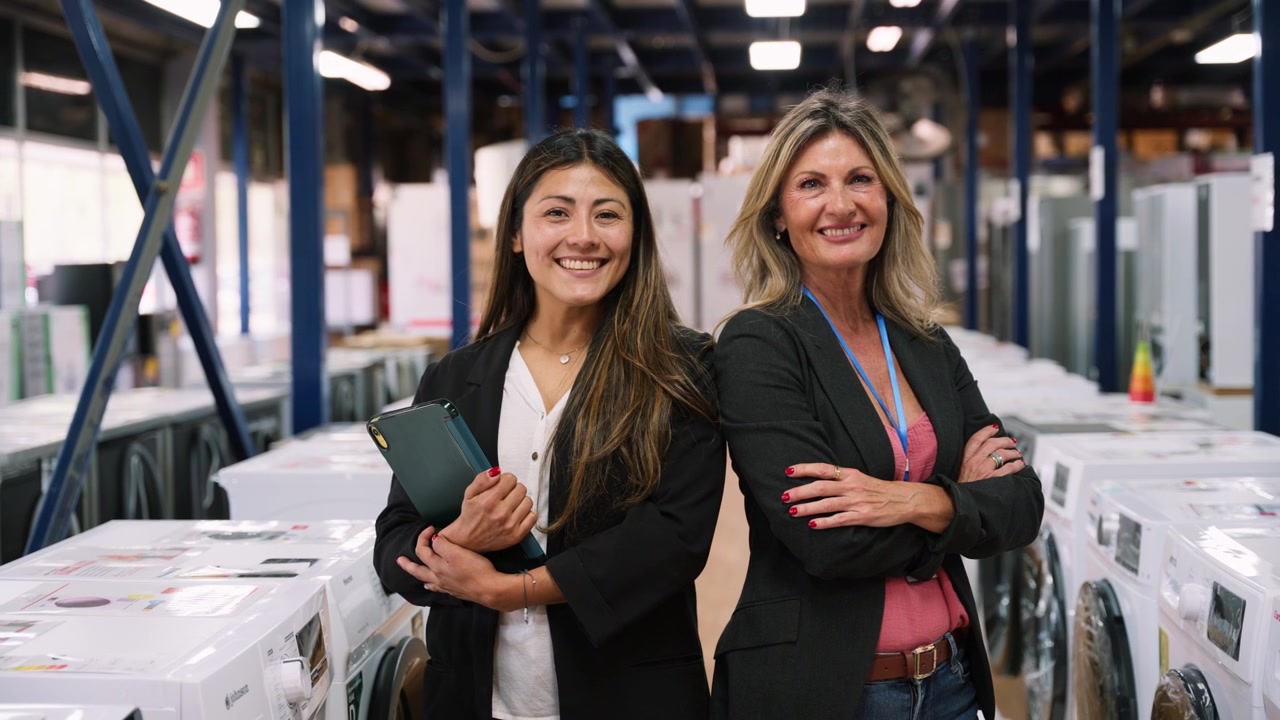 Dos mujeres profesionales sonriendo en un almacén lleno de electrodomésticos