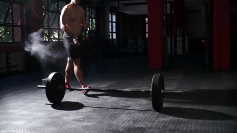 Bare-chested-man-preparing-to-lift-barbells-in-a-gym