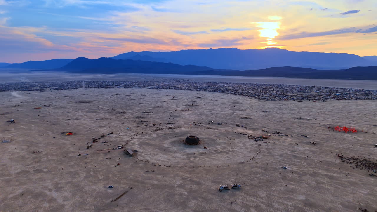 Ampla imagem aérea de cidade temporária no deserto. Vista panorâmica de um assentamento circular e estrutura central ao pôr do sol.