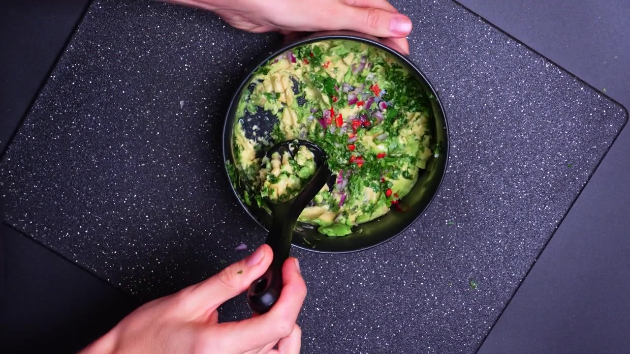 Preparazione di un piatto verde con ingredienti freschi su un piano di lavoro scuro. Mani mescolano erbe tritate e verdure in una ciotola su un piano di lavoro della cucina.