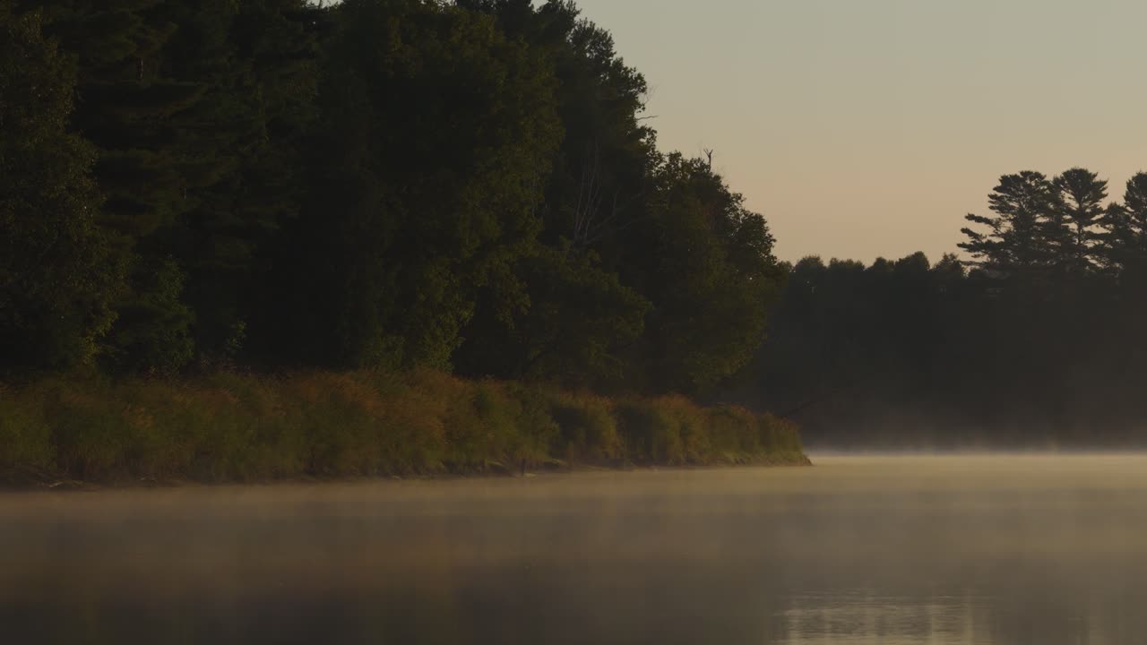 A flat stretch of Canada's Gatineau River in the morning mist, colored yellow by the sun