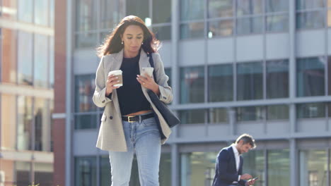 Mujer-De-Negocios-Con-Café-Para-Llevar-Caminando-A-La-Oficina-Mirando-El-Teléfono-Móvil