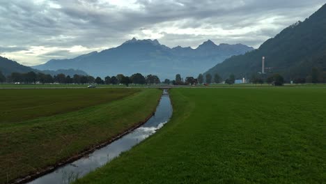 Aerial-flight-over-tranquil-stream-and-driving-cars-in-swiss-mountains-during-cloudy-day