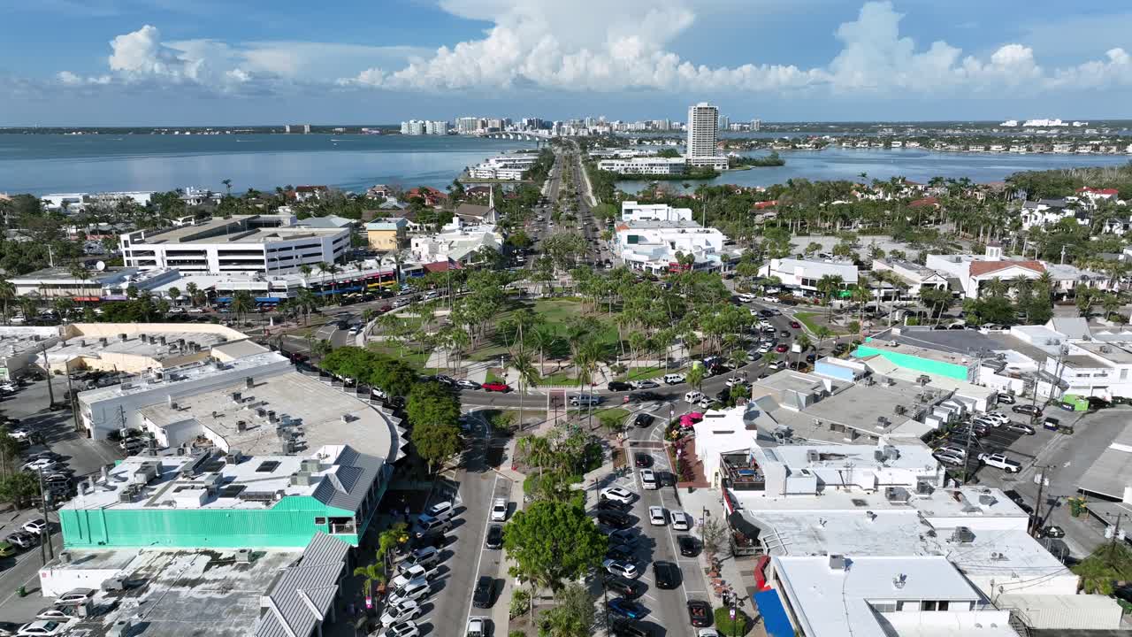 Lively aerial view of St. Armands Circle in Sarasota, Florida. Palm-lined roads, boutique shops, restaurants, and coastal scenery create a vibrant shopping and tourist destination near the Gulf Coast.