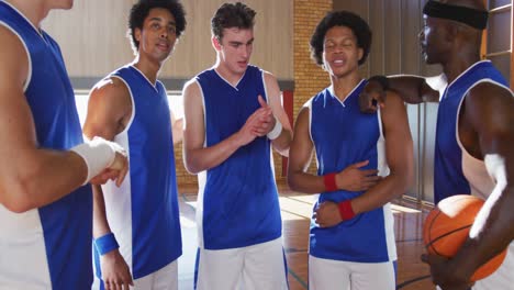 Diverse-male-basketball-team-and-coach-in-huddle-discussing-game-tactics