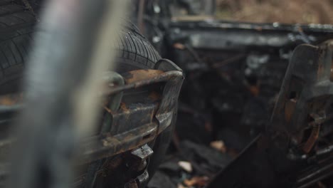 interior of burned out car with tire on rusted seat, closeup handheld detail pan