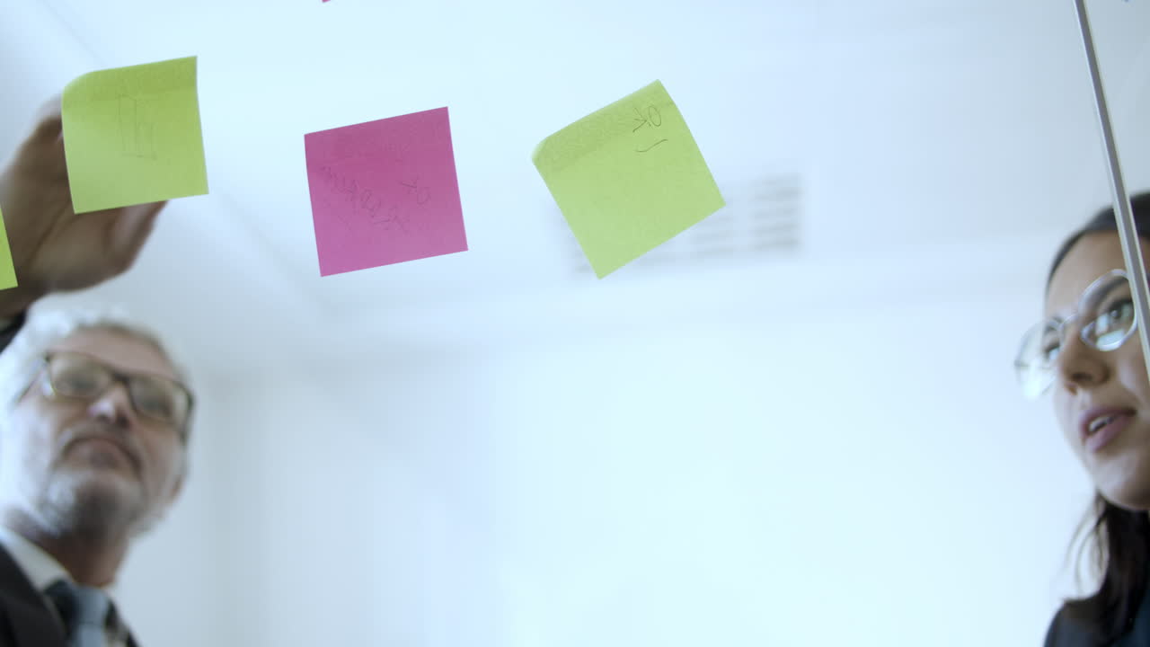Female marketing expert sticking notes on glass board next to her teammate