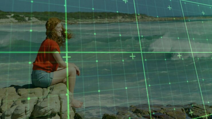 woman sitting on rock facing sea, starting green grid scanning shore for tech mapping