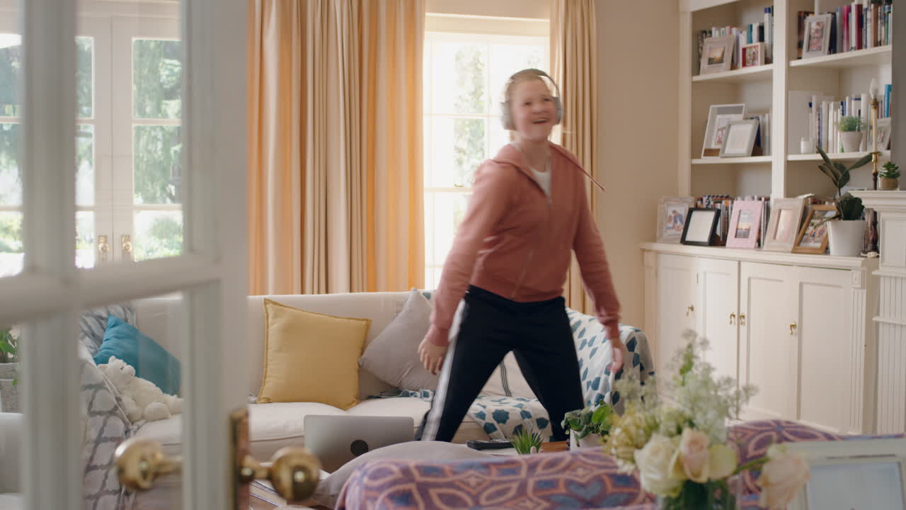 멋진 십대 소녀가 헤드폰을 착용하여 춤을 추고 음악을 듣고 재미있는 십대 소녀가 집에서 미친 춤 움직임으로 축하하고 주말에 자유를 즐기고 4k