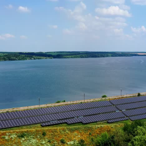 Solar panels on nature background. Blue sunny batteries on field near the river in summer. Solar farm near water. Aerial view