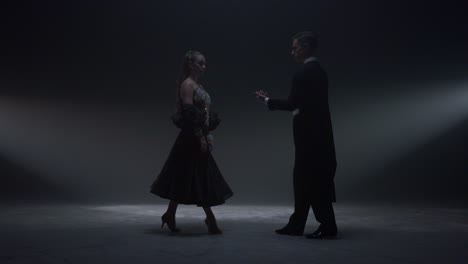 dance couple holding hands on dark stage. man inviting woman to dance indoors.