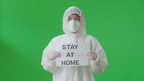 person in protective gear holding a sign that says 'stay at home'