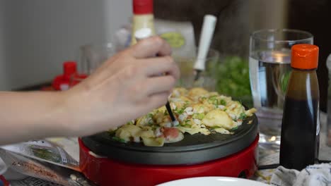 Takoyaki-being-cooked-at-home,-Hand-tends-to-Dumplings-on-Hot-Grill