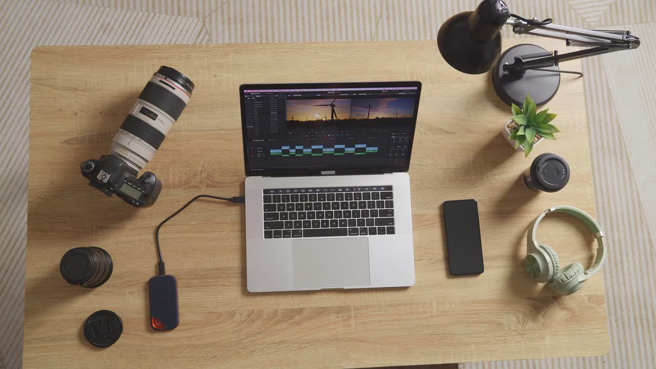 vista superior zoom out toma de una computadora portátil que muestra la edición de video en la mesa con teléfono inteligente y cámara en el espacio de trabajo en casa