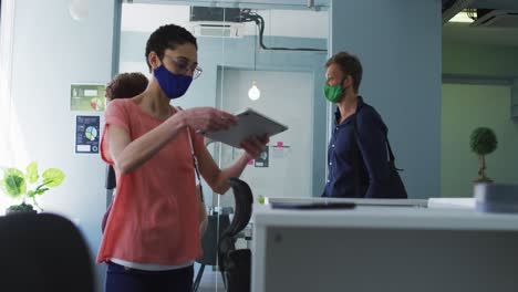 African-american-woman-wearing-face-mask-measuring-of-her-male-colleague-at-modern-office