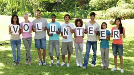 Group-of-casual-young-friends-smiling-at-camera-holding-letters-spelling-volunteer-