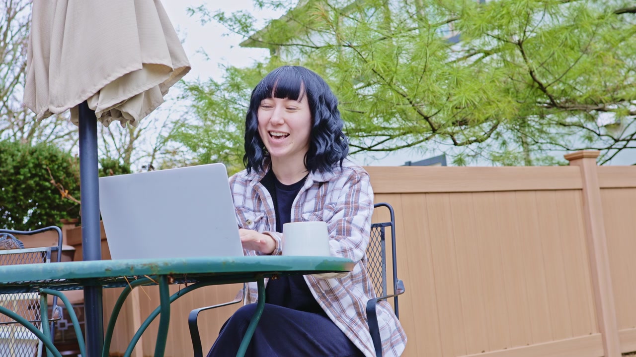 晴れた日に庭で、笑顔でコーヒーを楽しみながら屋外でノートパソコンで作業する女性