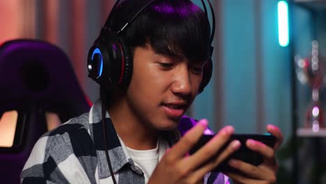 close up of excited asian teen boy gamer celebrates victory while playing video game on smartphone