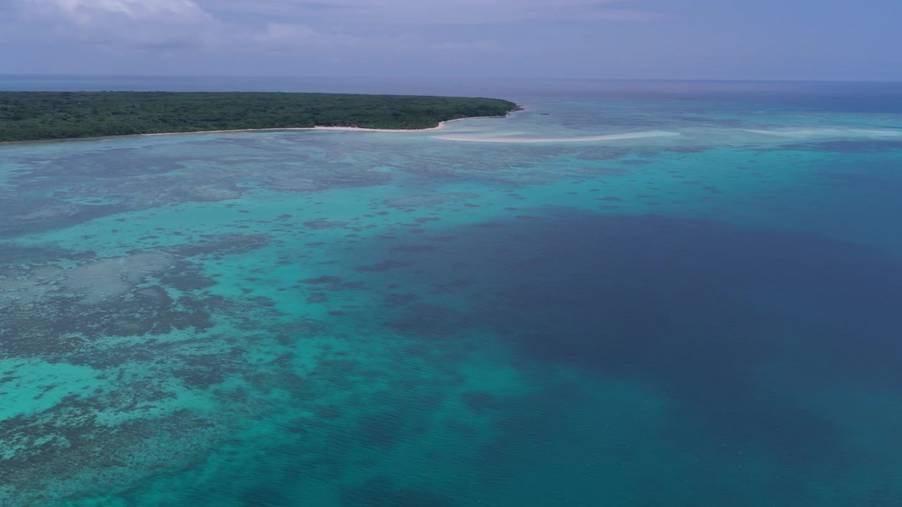 Riprese aeree orizzontali con panoramica verso sinistra e carrellata verso destra sopra la laguna turchese e le barriere coralline del molo di Nishi e della spiaggia di Kondoi, Isola di Taketomi, Okinawa, Giappone.