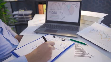 Businessman analyzing financial earnings and growth charts on laptop and paper.