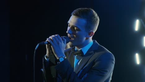 man singing song in microphone during performance on stage on rock concert. close up man rock star singer on music concert on colorful light background