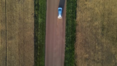 Aerial-vertical-shot-of-minivan-driving-along-dirt-road-in-rural-Canada