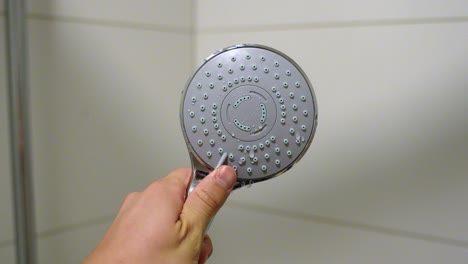 ajustar el flujo del cabezal de la ducha usando los pulgares desde el baño, pov estático