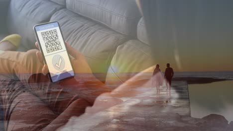 Animation-of-caucasian-woman-with-smartphone-with-covid-passport-over-couple-on-beach