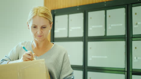 a woman writes an address on the parcel box in the post office