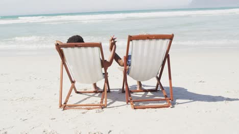 african american couple holding hands and lying on sunbeds on sunny beach