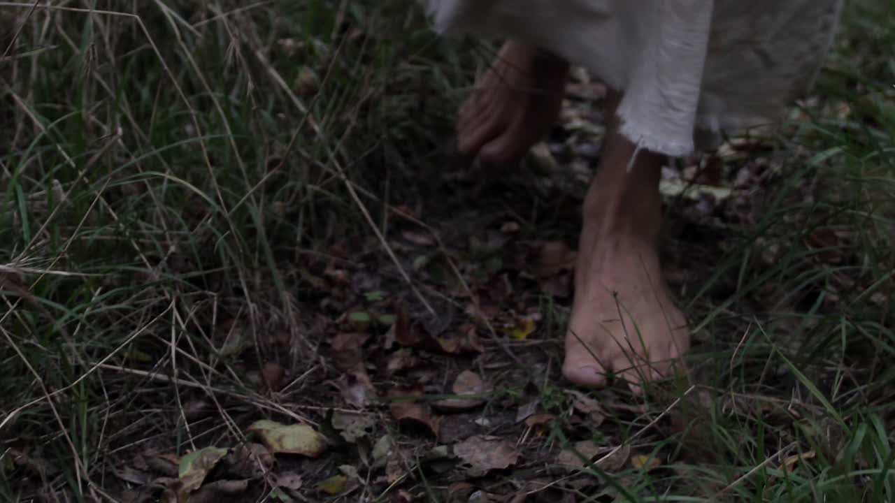 Closeup of feet of robed man or Jesus walking through forest trees in slow motion