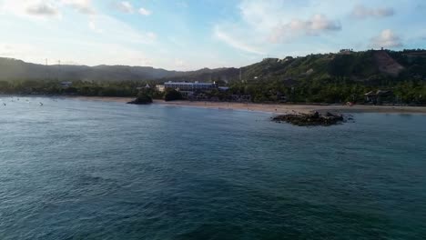drone video of kuta lombok bay at sunset – aerial flight over ocean toward beach with golden light, calm waves, and scenic coastline on indonesia’s southern shore
