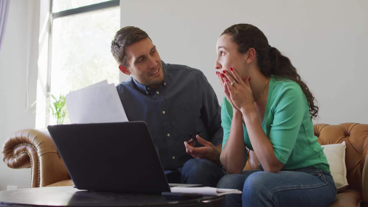 una joven pareja caucásica hablando y pagando sus cuentas usando una computadora portátil