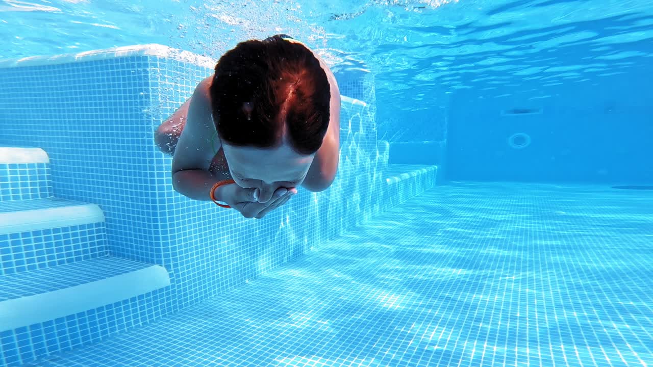 A young guy swims underwater in a swimming pool on a blue background. Underwater video.