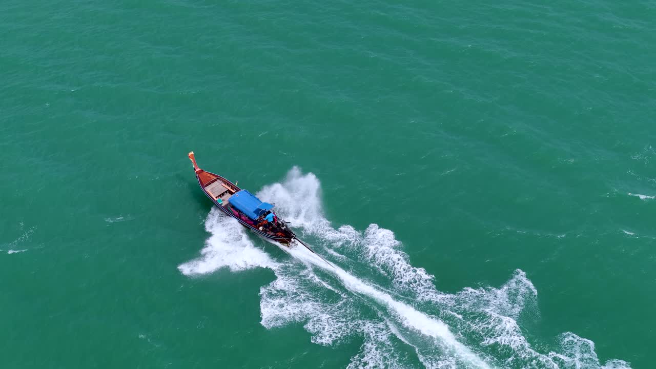 Pemandangan udara sudut tinggi sebuah perahu ekor panjang tradisional yang melaju melintasi air laut tropis biru kehijauan yang jernih.