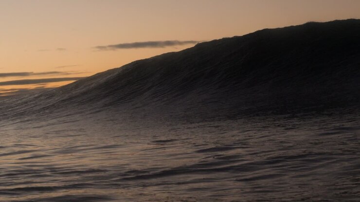 A short heavy wave crash over the shallow rock ledge as the sun rises in the background