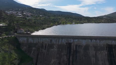 lateral drone flight along a fully loaded dam wall. sunlight reflects on the water's surface as we move, ending over a lush green area with two visible crossing paths.