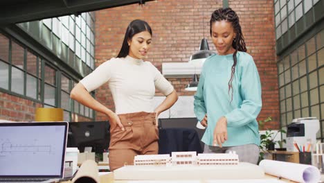 mujeres arquitectas felices y diversas mirando modelos arquitectónicos en la oficina