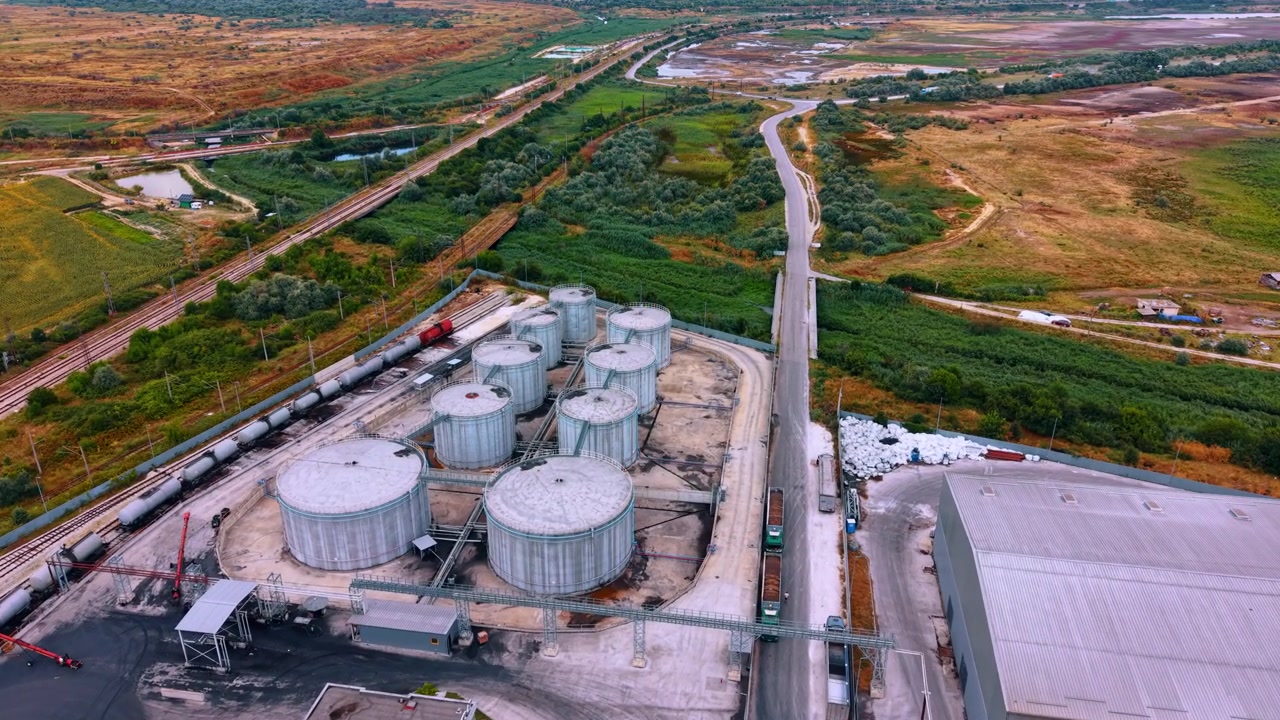 Serbatoi di stoccaggio vicino ai binari ferroviari in un'area industriale. Serbatoi di stoccaggio si trovano in un'area industriale accanto a binari ferroviari e campi. Camion si muovono in entrata e in uscita mentre il sole tramonta.